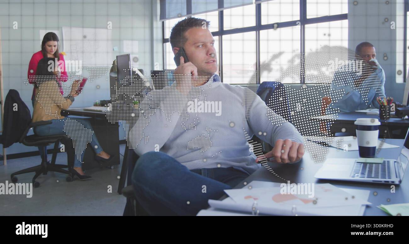 Rispondere a un uomo di mezza età che parla su smartphone in un ufficio aperto con monitor, laptop e mappa del mondo Foto Stock