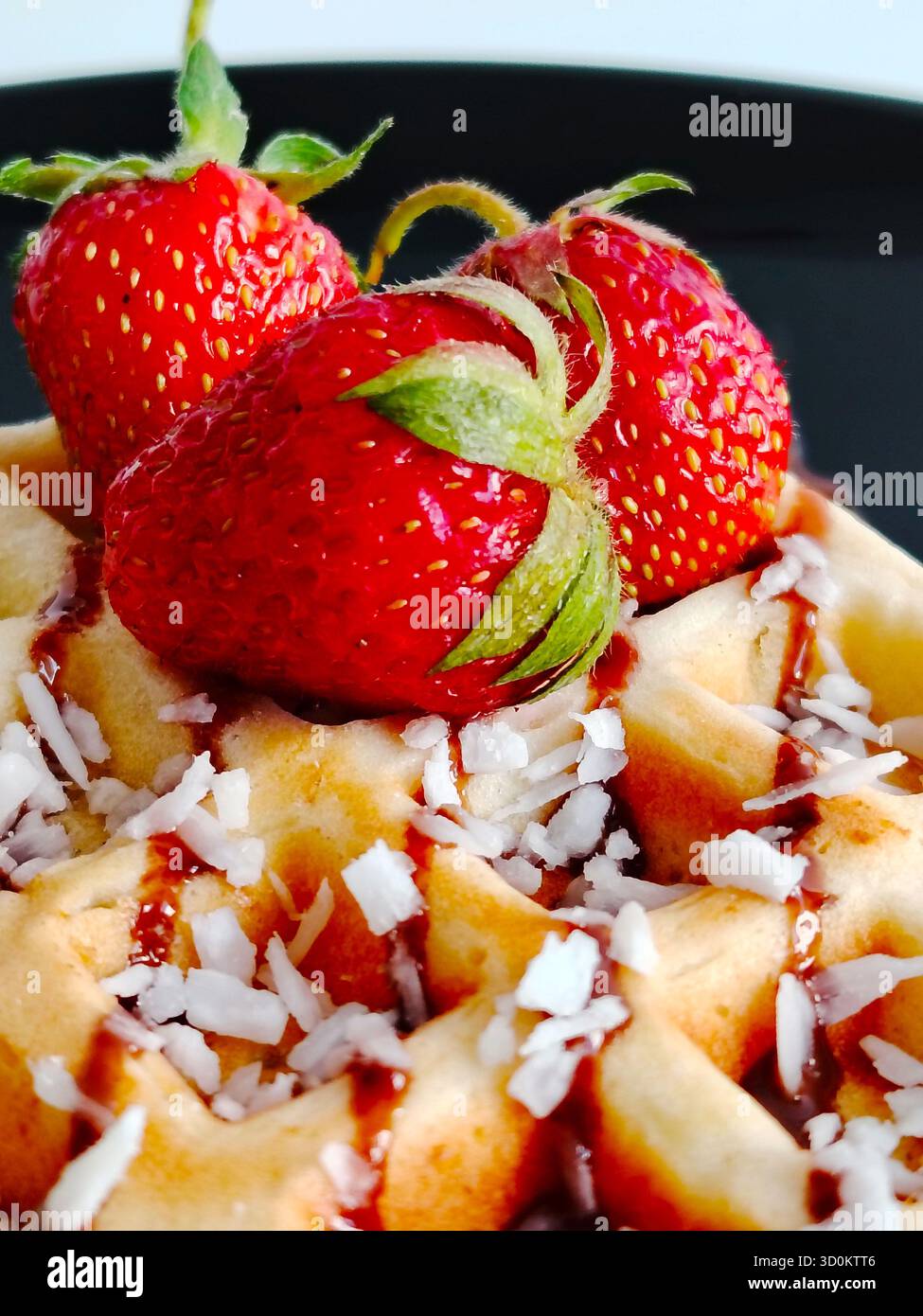 Primo piano di waffle con scaglie di cocco, fragole e sciroppo al cioccolato. Foto Stock