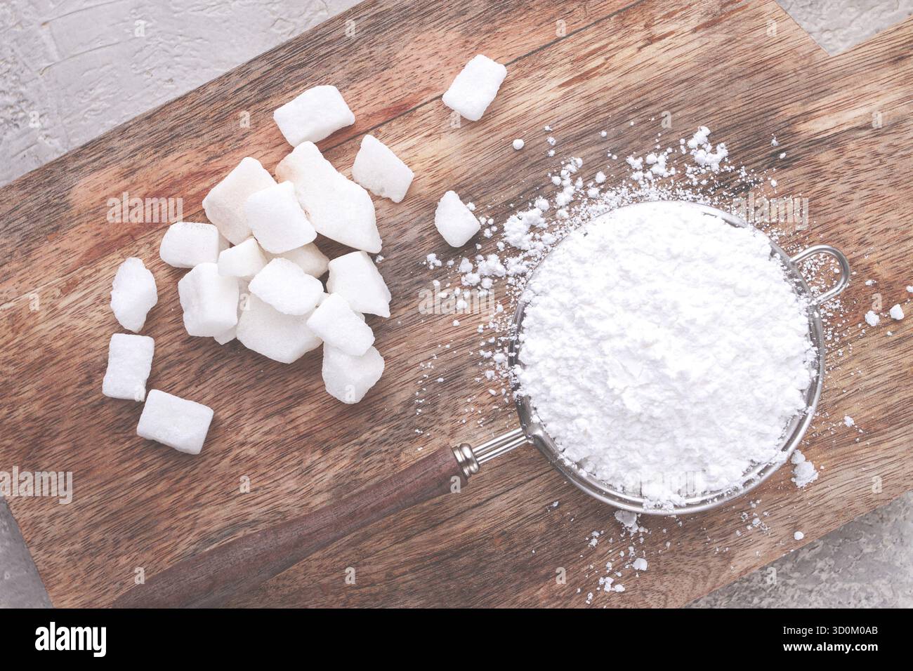 Un filtro con zucchero a velo, su un tagliere di legno, con pezzi di zucchero bianco Foto Stock