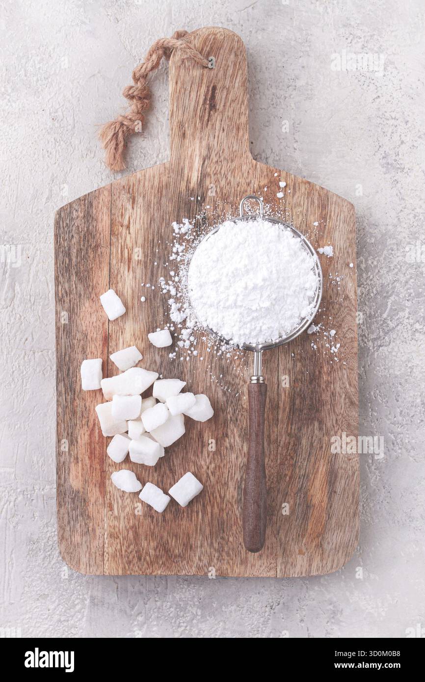 Un filtro con zucchero a velo, su un tagliere di legno, con pezzi di zucchero bianco Foto Stock