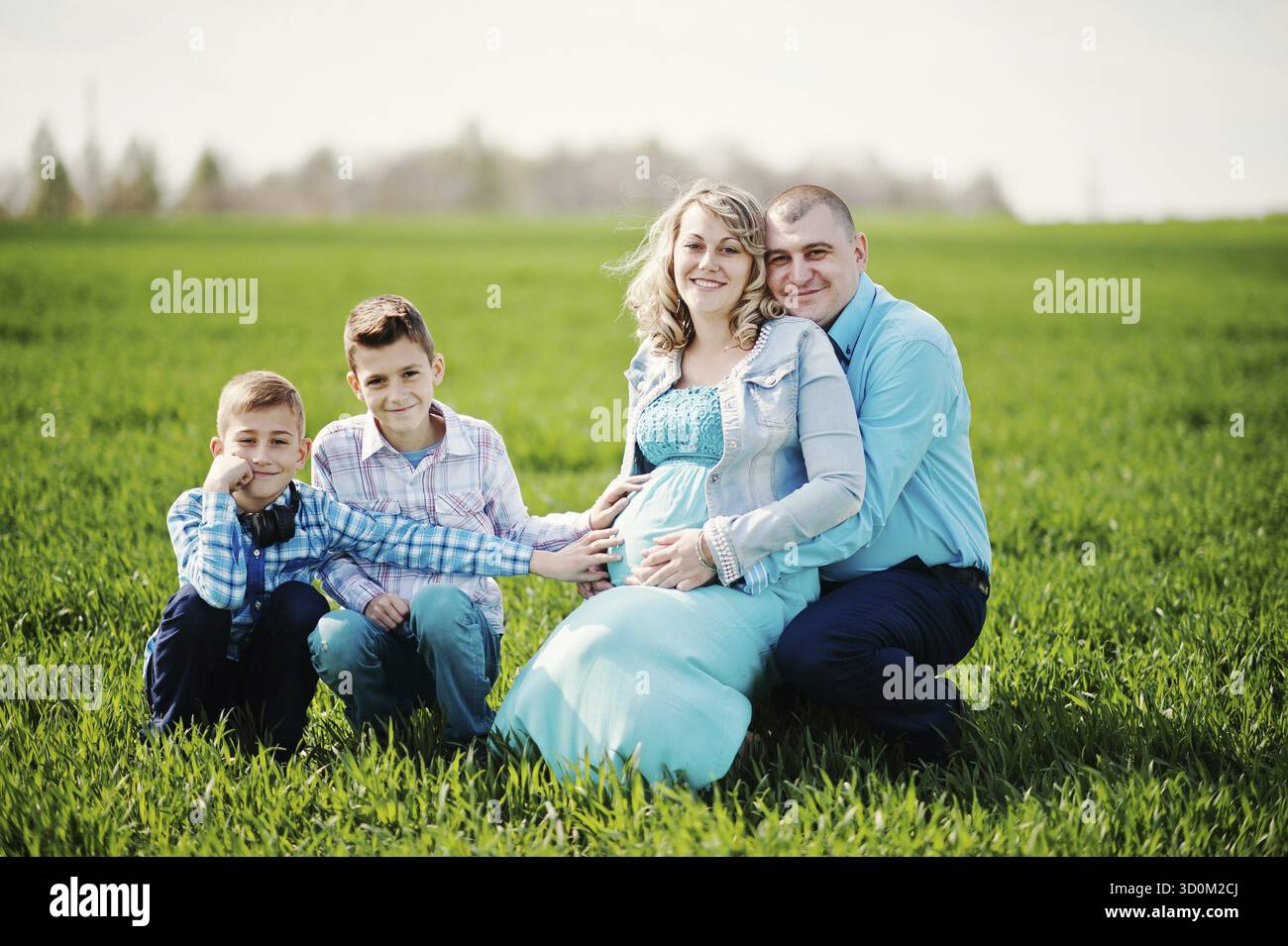 Gravidanza felice famiglia con due figli, vestito di un turchese vestiti, trascorrere del tempo insieme a erba verde nel campo Foto Stock