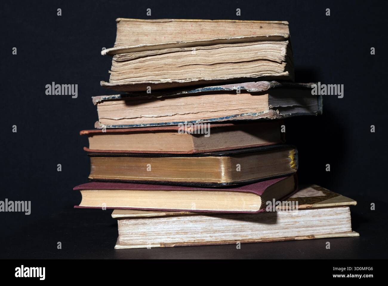 Una pila alta e irregolare di libri in copertina rigida antichi e vintage. L'immagine evidenzia i bordi della pagina diversi e molto usurati (bordi anteriori). Foto Stock
