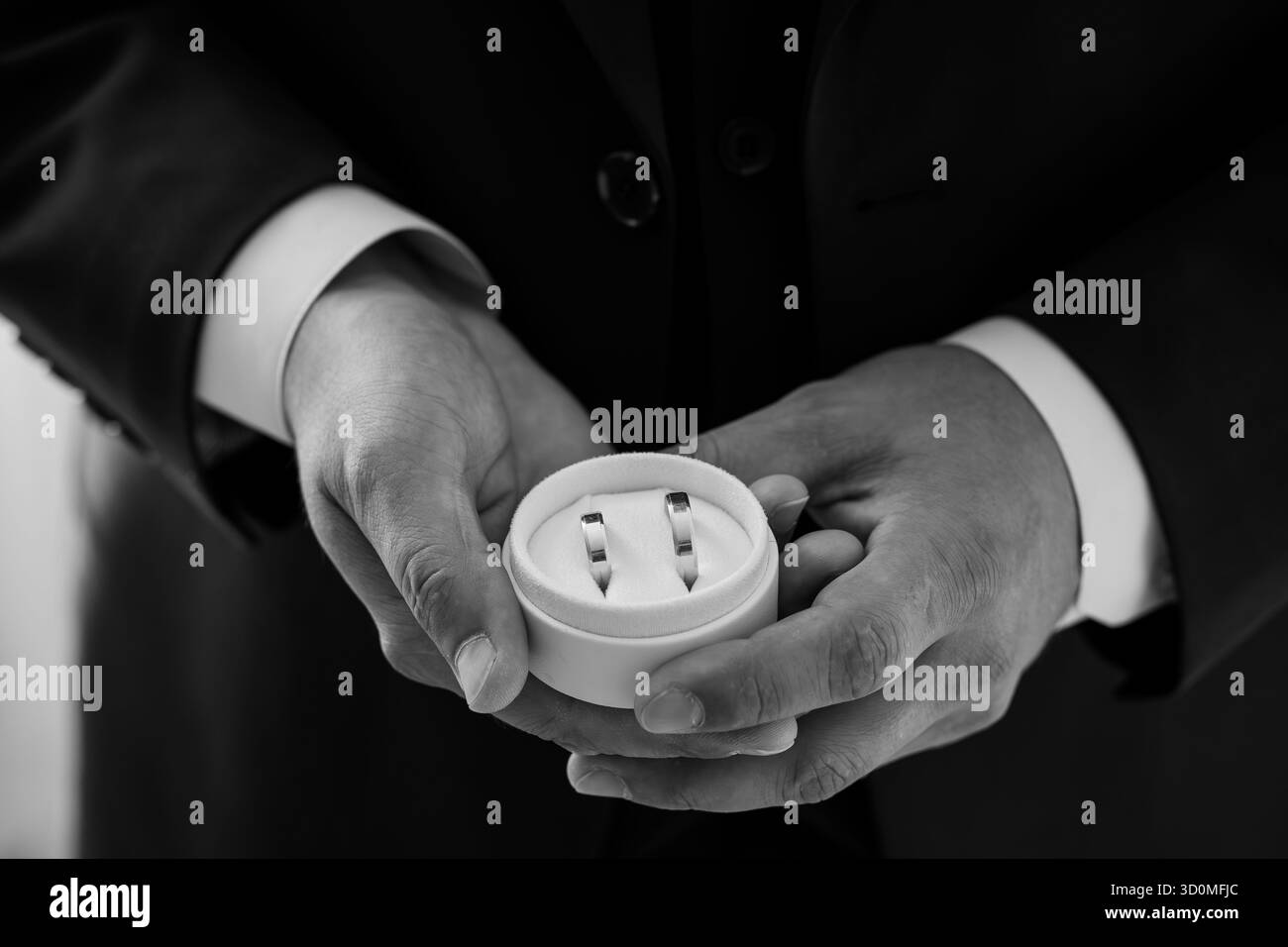 Un primo piano di uno sposo in uno smoking che presenta una scatola anello contenente le feste nuziali, simboleggiando l'amore, l'impegno e l'anticipazione del matrimonio. Foto Stock