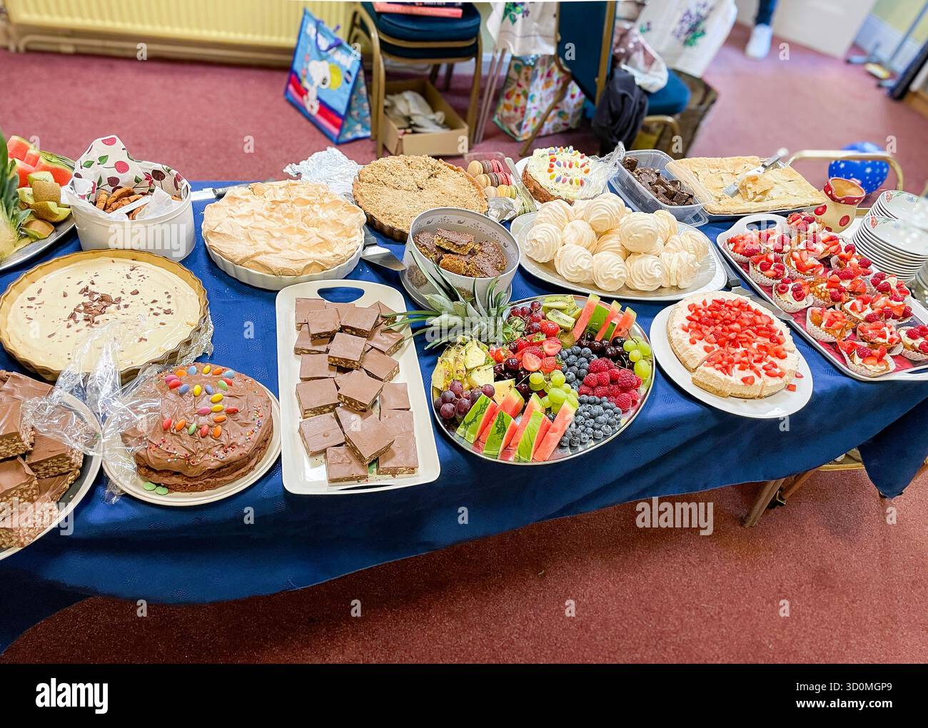 Tavolo ripieno di un'ampia varietà di dessert fatti in casa, tra cui torte, torte, vassoi di frutta e dolci durante una festa al coperto - Immagine stock catturata con smartphone