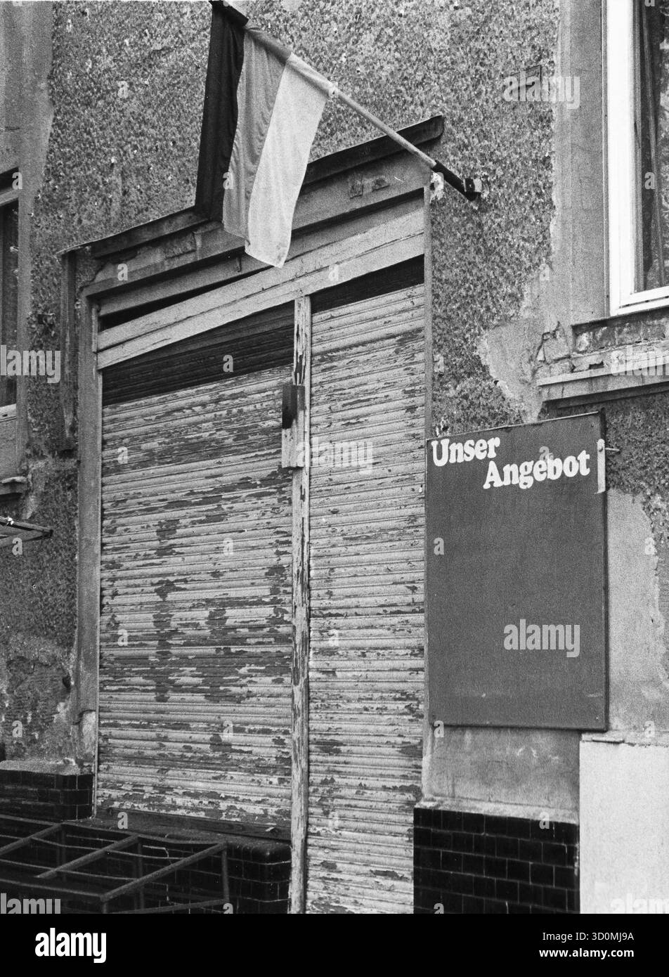 DEU, Germania, Berlino, 1990-03-18: Un negozio di alimentari in rovina nel quartiere Heinersdorf del quartiere berlinese di Pankow, appena un quarto di anno dopo l'apertura del muro di Berlino. Le tende del negozio sono abbassate, la tavola accanto all'ingresso con la scritta "Unser Angebot" (la nostra offerta) è vuota. Una bandiera tedesca è appesa sulla facciata in brollizione. HF [traduzione automatizzata] Foto Stock