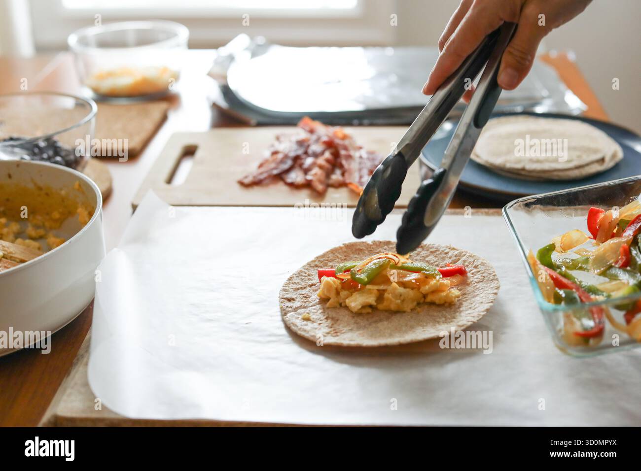 La donna mette i peperoni sulla tortilla per preparare i pasti per i burritos della colazione Foto Stock