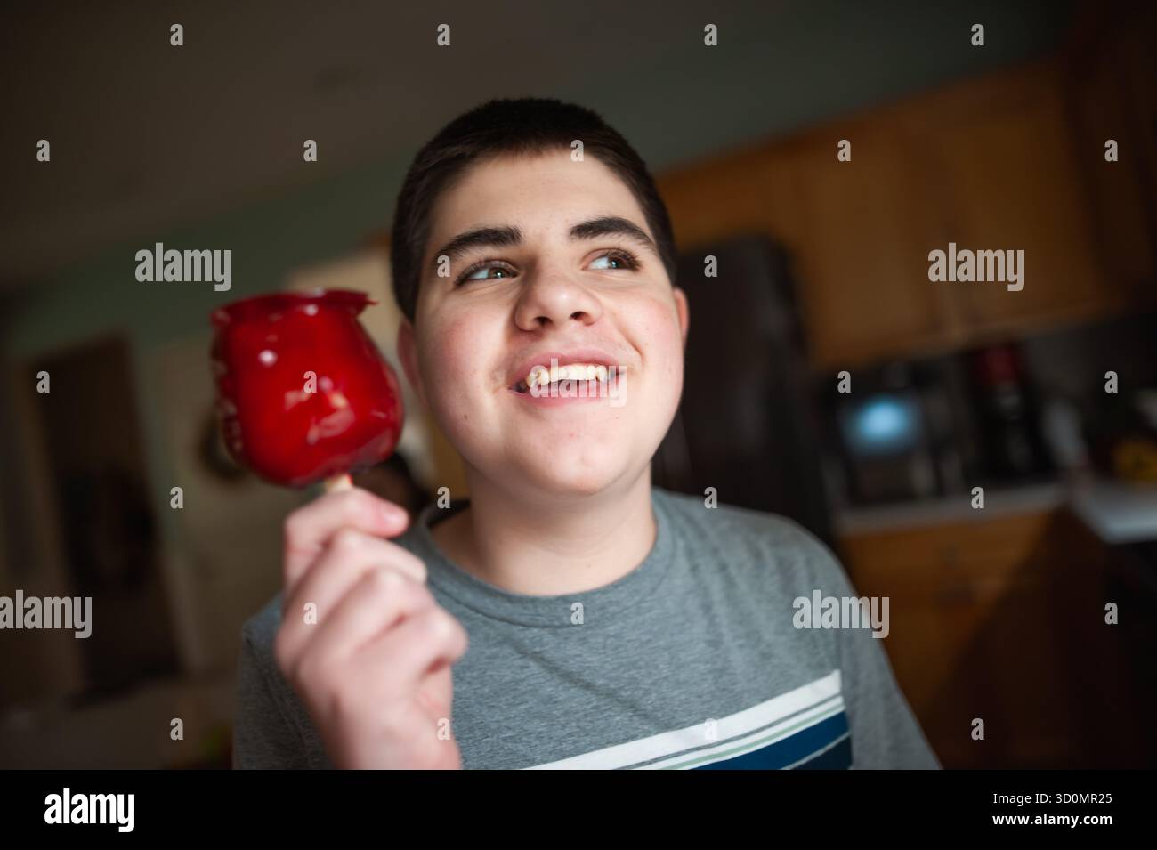 Un adolescente allegro che tiene in mano mele rosse caramelle in un'accogliente cucina Foto Stock