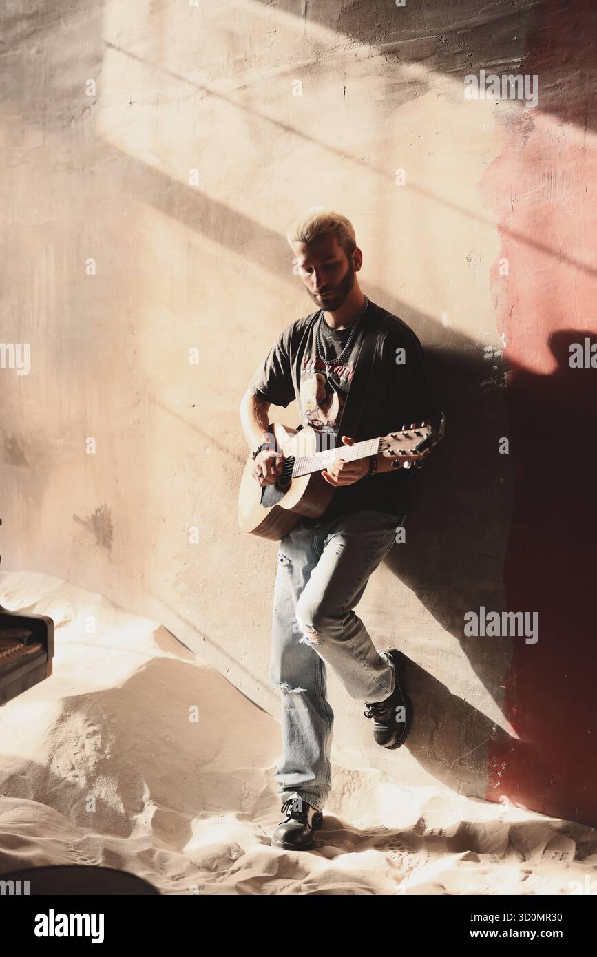 Il musicista suona la chitarra contro una parete testurizzata con un'illuminazione soffusa Foto Stock