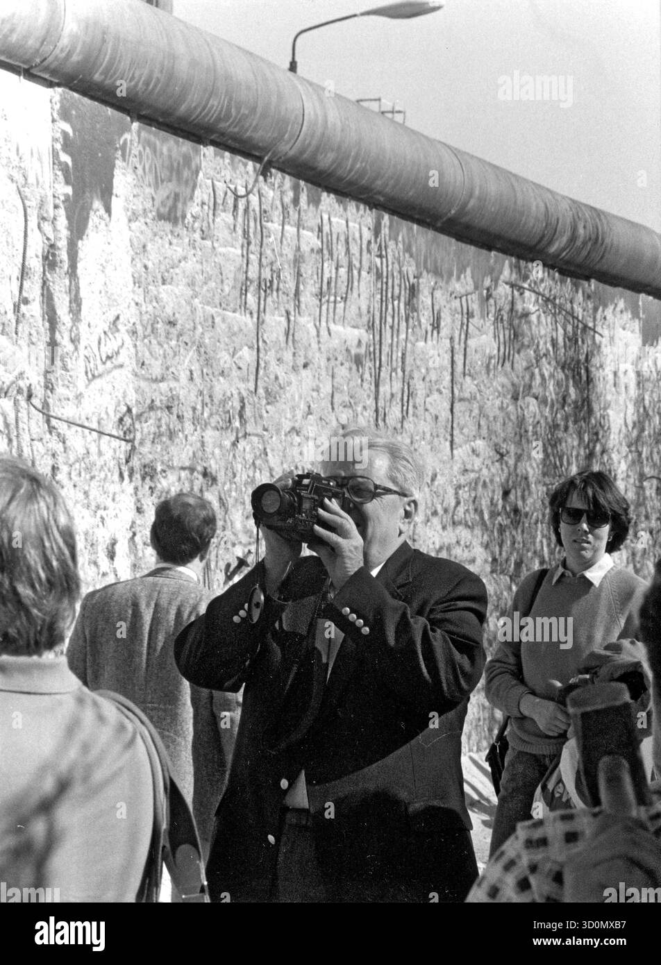 DEU, Germania, Berlino, 1990-03-18: Non lontano dal Checkpoint Charlie, l'ambasciatore americano Vernon Walters filma un video del muro dipinto da picchi. HF [traduzione automatizzata] Foto Stock
