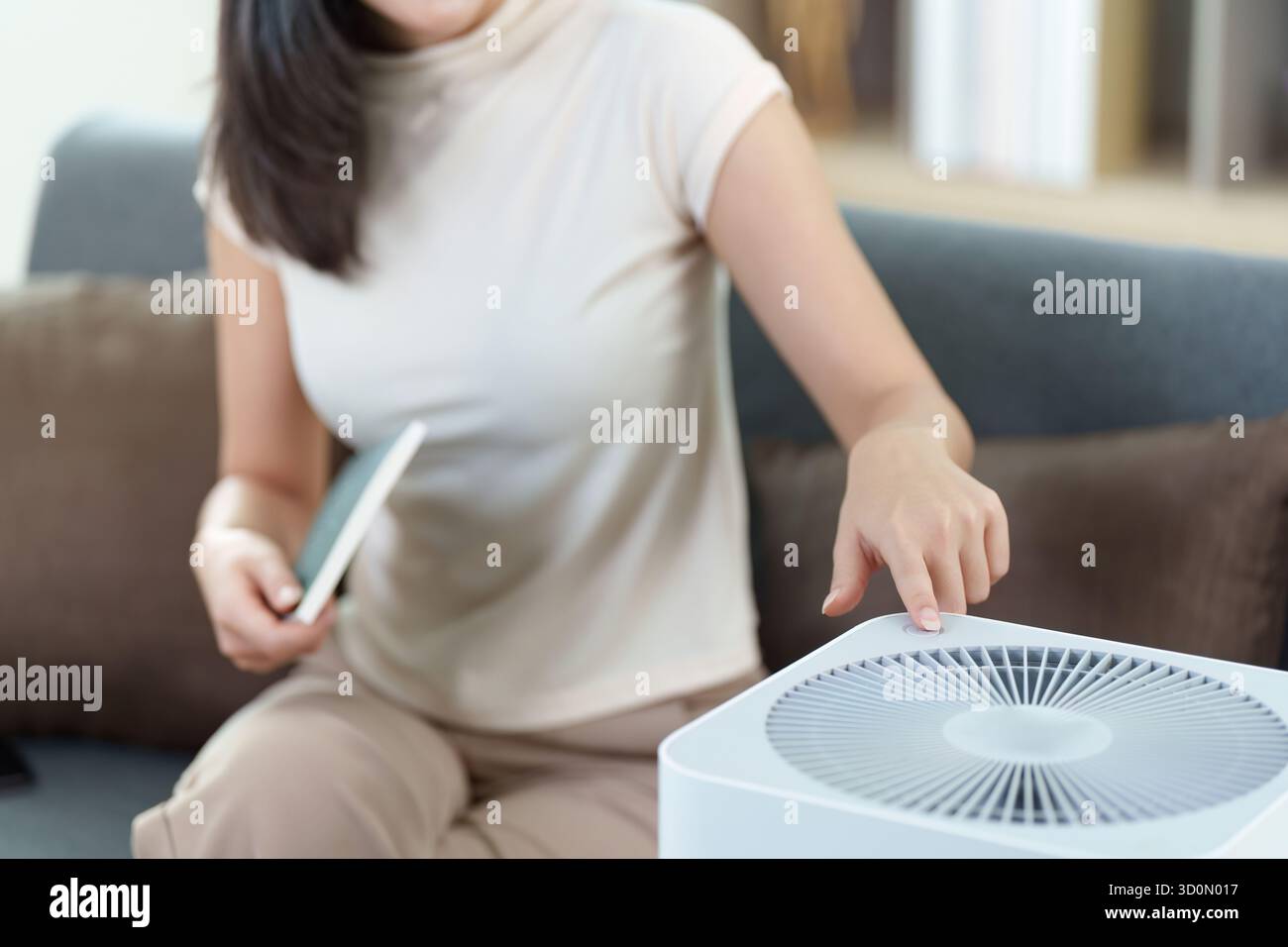 Casa intelligente. Donna che controlla il purificatore d'aria con smartphone in un salotto moderno. Foto Stock