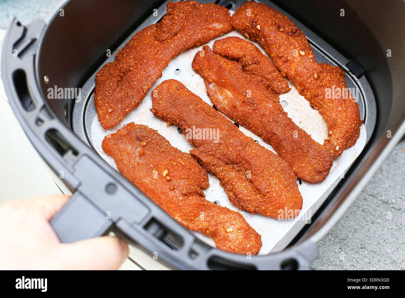 Filetti di pollo marinato crudi nel cestello della friggitrice ad aria. Preparazione del pollame prima della cottura. Carne di pollo condita pronta per la frittura. Preparazione degli alimenti da cucina. Foto Stock