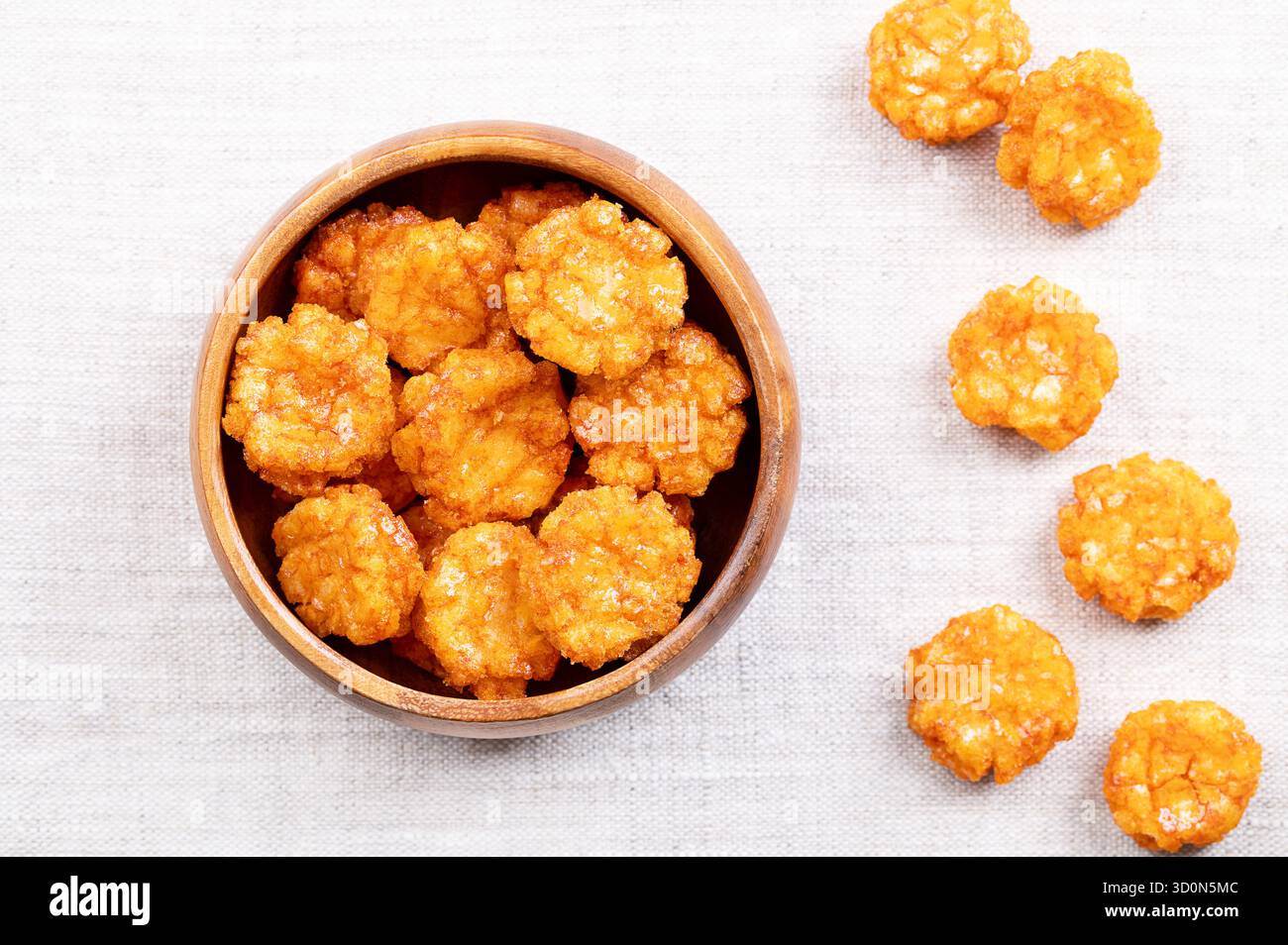 Cracker di riso al peperoncino tailandese in una ciotola di legno su tessuto di lino. Croccanti caldi, dolci e piccanti, uno spuntino a base di riso, condito con peperoncino in polvere. Foto Stock