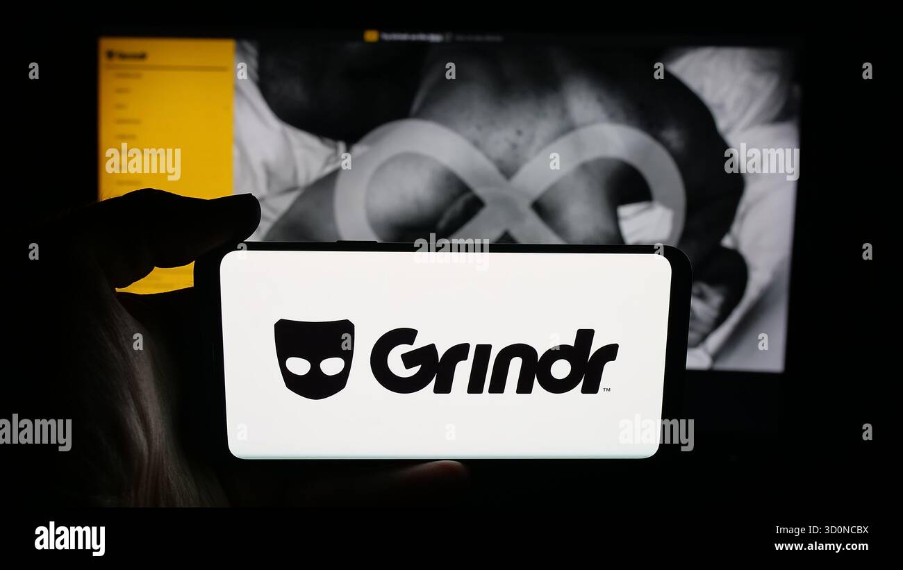 Stoccarda, Germania - 10-15-2025: Persona che tiene il cellulare con il logo della società di social media LGBT Grindr Inc sullo schermo davanti alla pagina web. Fil Foto Stock
