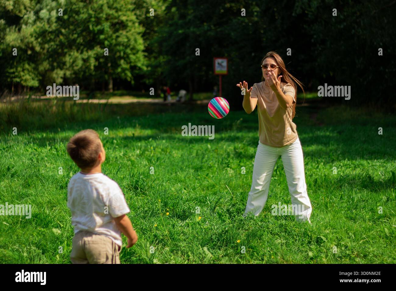 Mamma e bambino giocano a palla insieme nella natura durante le vacanze estive. Giocare a palla con il figlio nel parco. Palla presa Foto Stock