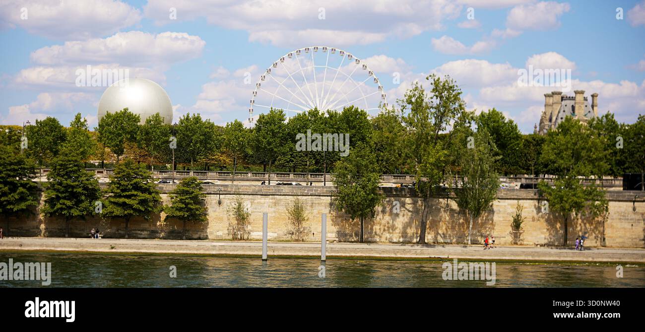 Immagine editoriale della sponda del fiume di Parigi con ruota panoramica, cupola d'argento e parte del Palazzo del Louvre visibile sopra una linea di alberi verdi in un pomeriggio di sole, scattato il 20 luglio 2025. Foto Stock