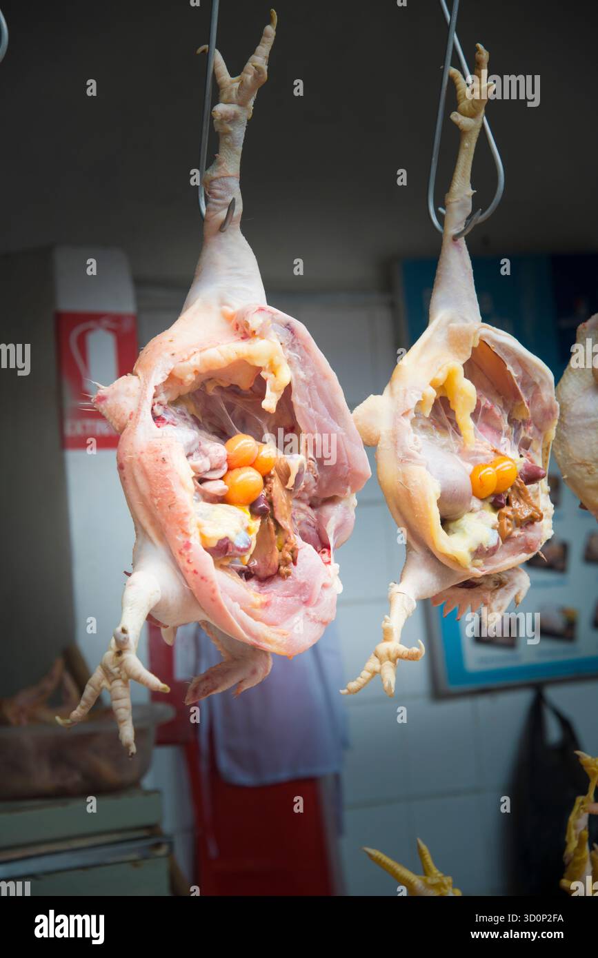 Due polli interi con uova interne appese in un mercato Foto Stock