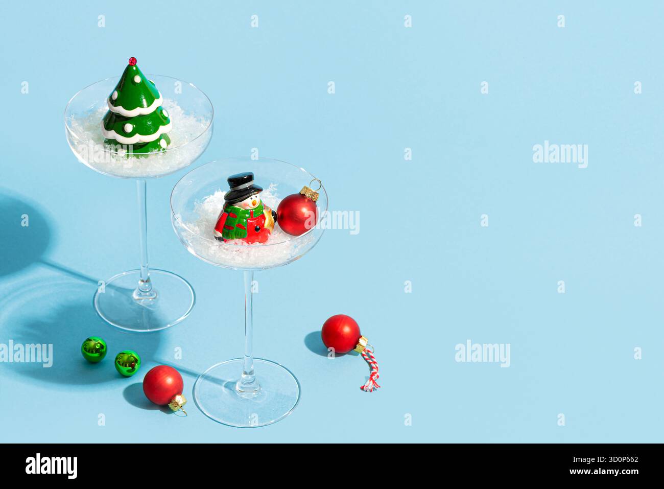 Albero di Natale e pupazzo di neve in bicchieri cocktail Martini su sfondo blu, spazio copia, luce solare alla moda. Concept design creativo per la festa di Natale. Foto Stock