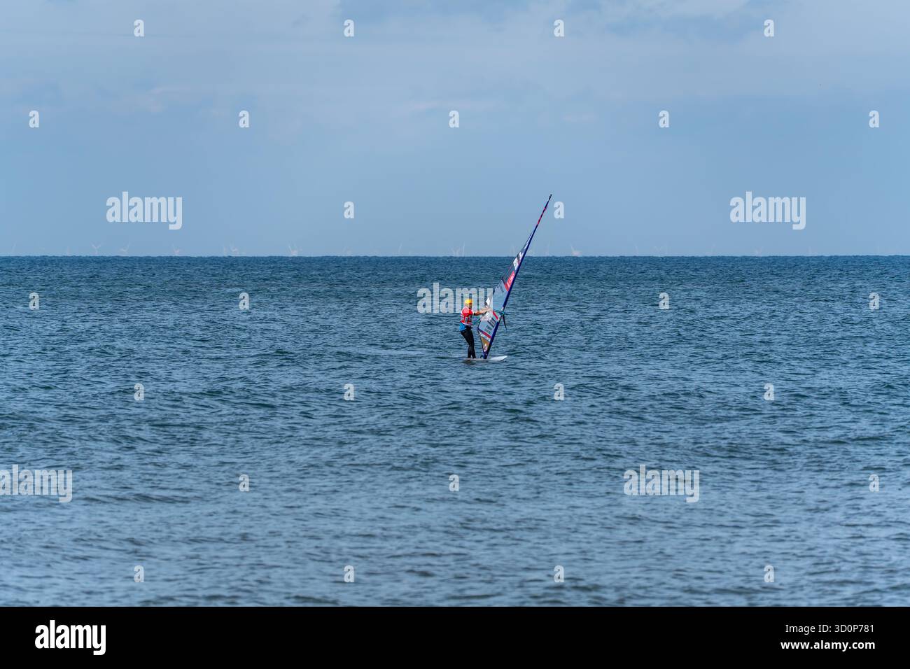 Germania Sylt 2 ottobre 2025. Un windsurfista solitario si bilancia sulle onde sotto un cielo limpido. Turbine eoliche distanti allineano l'orizzonte. Foto Stock