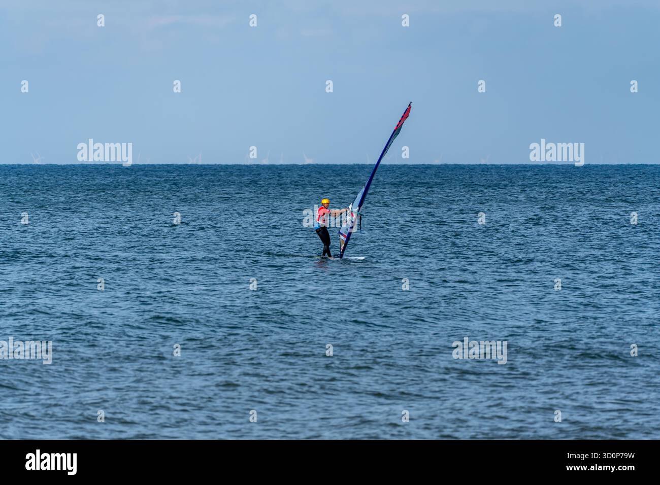 Germania Sylt 2 ottobre 2025. Il windsurfer scivola costantemente sul mare, incorniciato da turbine lontane. Un momento di concentrazione e flusso sul wate aperto Foto Stock