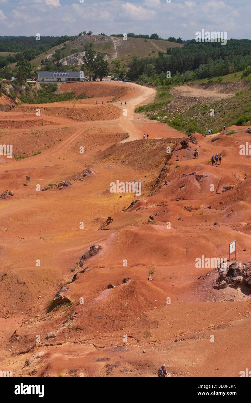 I visitatori camminano tra le colline rosse della miniera di Gánt Bauxite in un giorno d'estate soleggiato, in Ungheria. Foto Stock