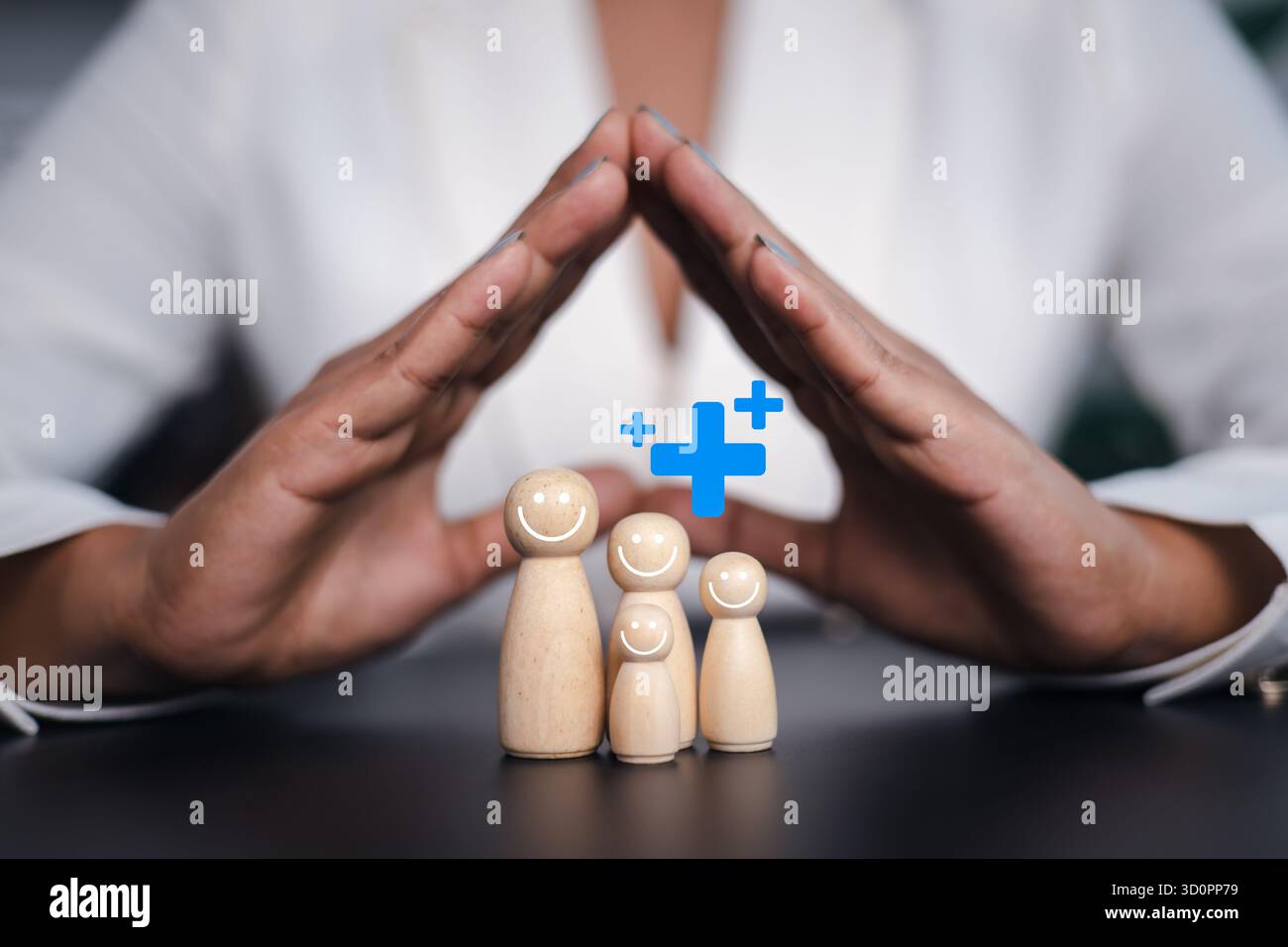 Mani che proteggono figure familiari in legno con icona croce medica, concetto di assicurazione sanitaria familiare, sicurezza, benessere e protezione sanitaria. Foto Stock