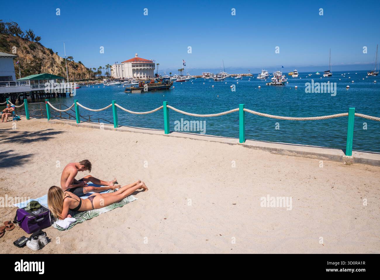 Avalon, Catalina Island, CA USA - 25 aprile 2019: Coppia che prende il sole sulla spiaggia di Step di fronte all'Arco del Casinò, lungo Crescent Avenue. Foto Stock