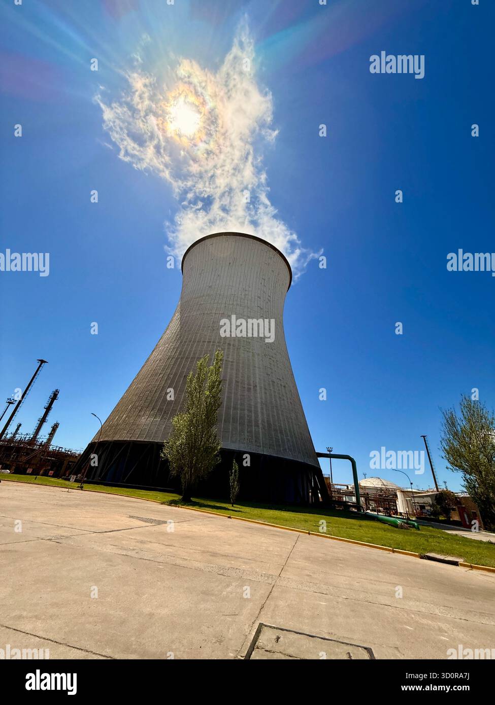 Torre di raffreddamento che emette vapore sotto alone solare presso l'impianto industriale - Immagine stock catturata con smartphone