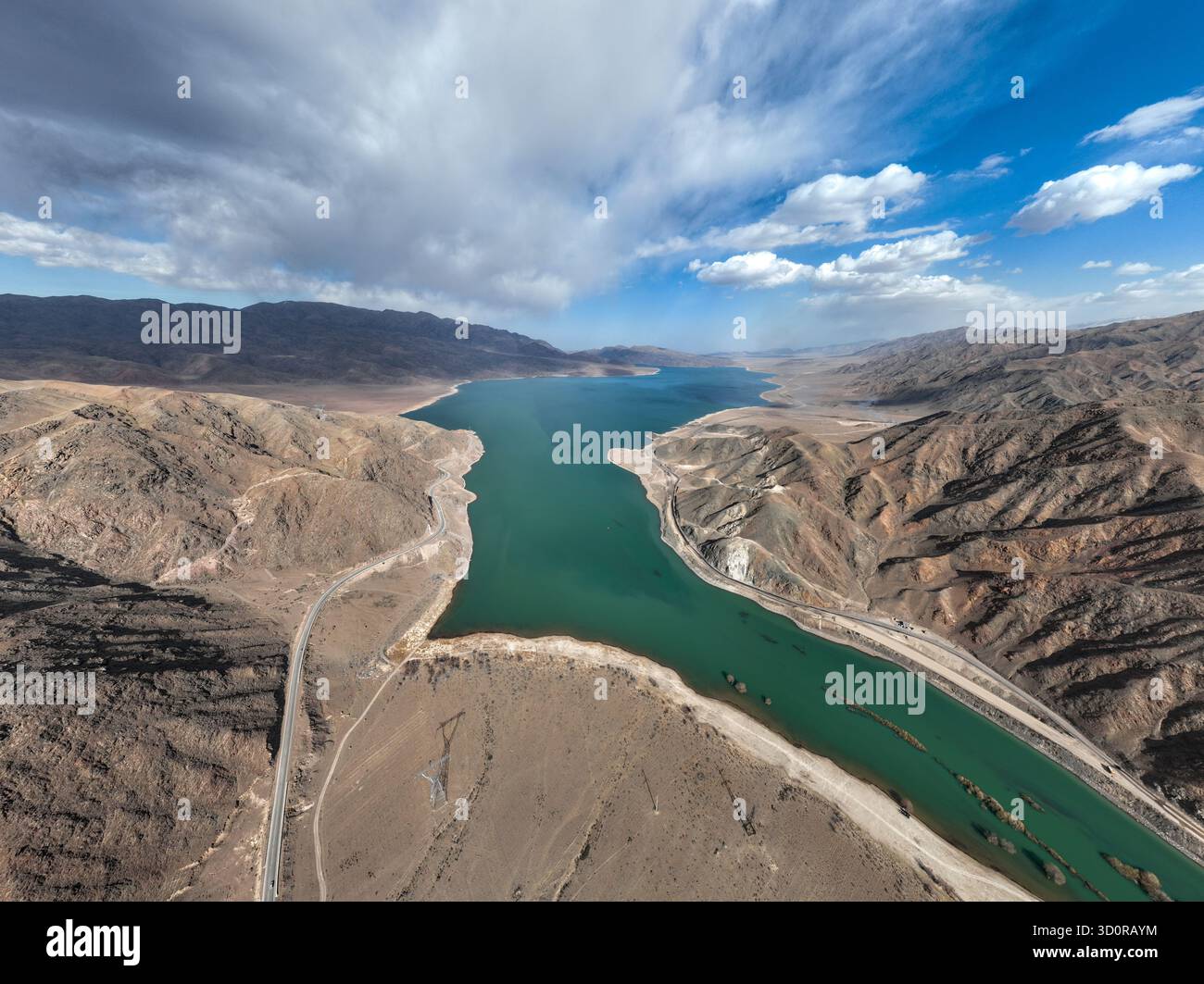 Ampia vista aerea di un vivace bacino idrico turchese che si estende attraverso un'ampia e arida valle di montagna sotto un cielo spettacolare con nuvole sparse Foto Stock