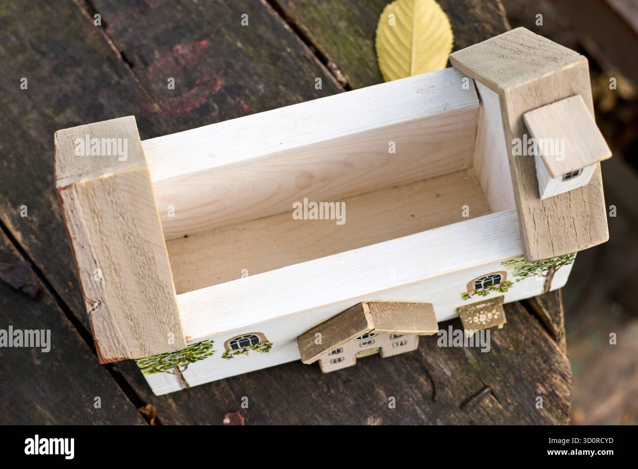 Un'affascinante scatola di legno progettata come una casa stravagante con dettagli dipinti, annidata su una superficie in legno intemprata sotto la luce naturale. Foto Stock