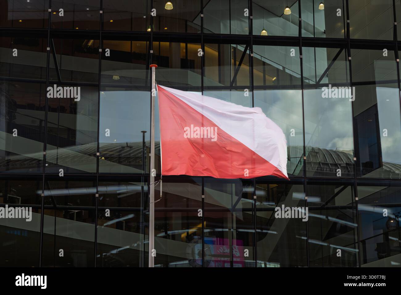 Bandiera provinciale olandese di Utrecht, caratterizzata da una croce diagonale bianca e rossa, che ondeggia su un palo di bandiera contro una moderna facciata di un edificio di uffici in vetro. Foto Stock