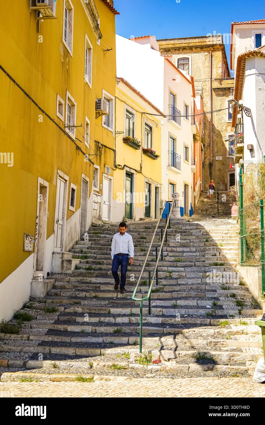 Lisbona, Portogallo – uomo che cammina lungo i gradini di pietra nel soleggiato quartiere di Grazia sotto il cielo blu. Foto Stock