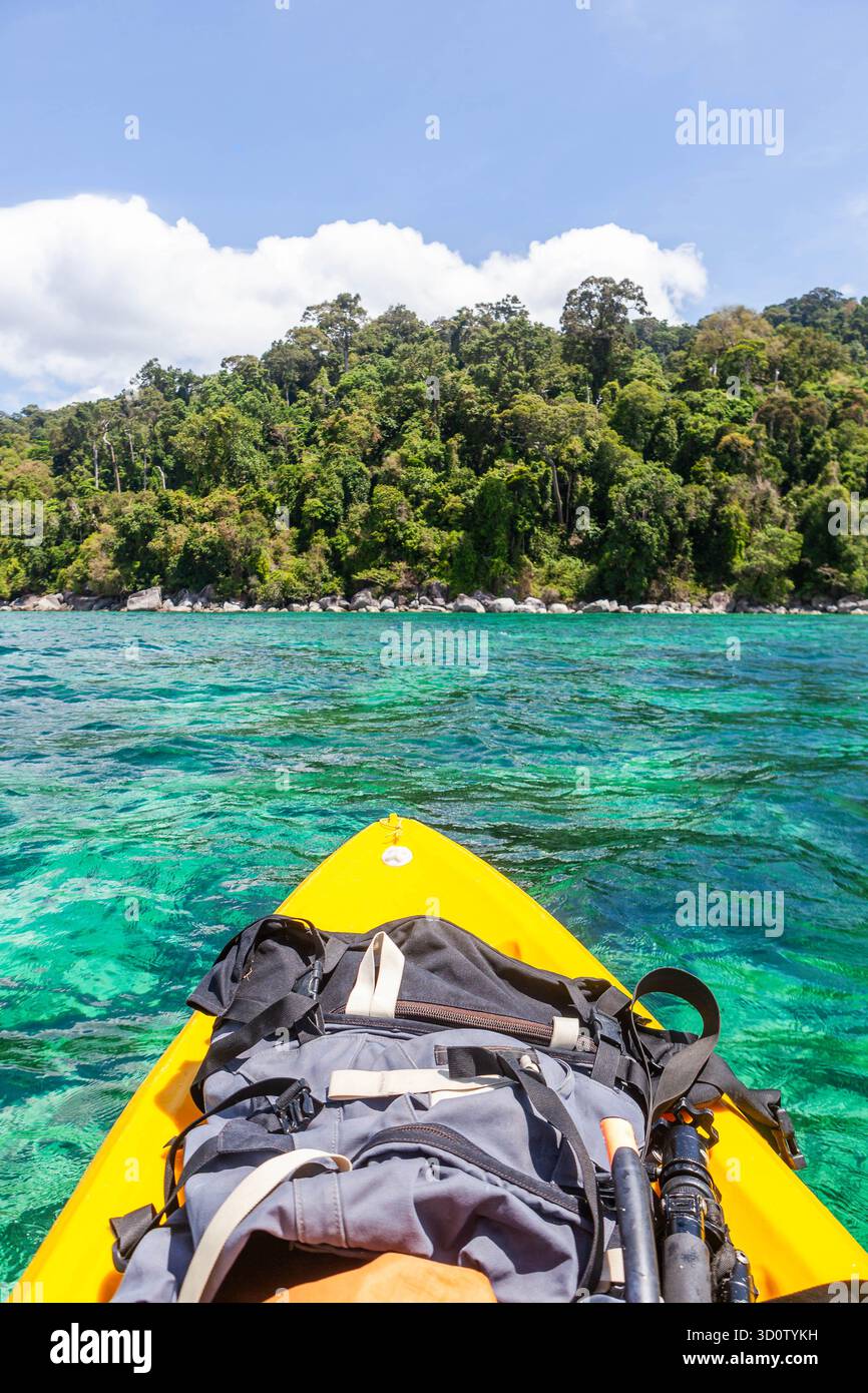 Ko Adang, Thailandia. Una vista in prima persona da un kayak giallo, pagaiando in acque cristalline color smeraldo vicino a una lussureggiante costa verde della giungla sotto la luce del sole. Foto Stock
