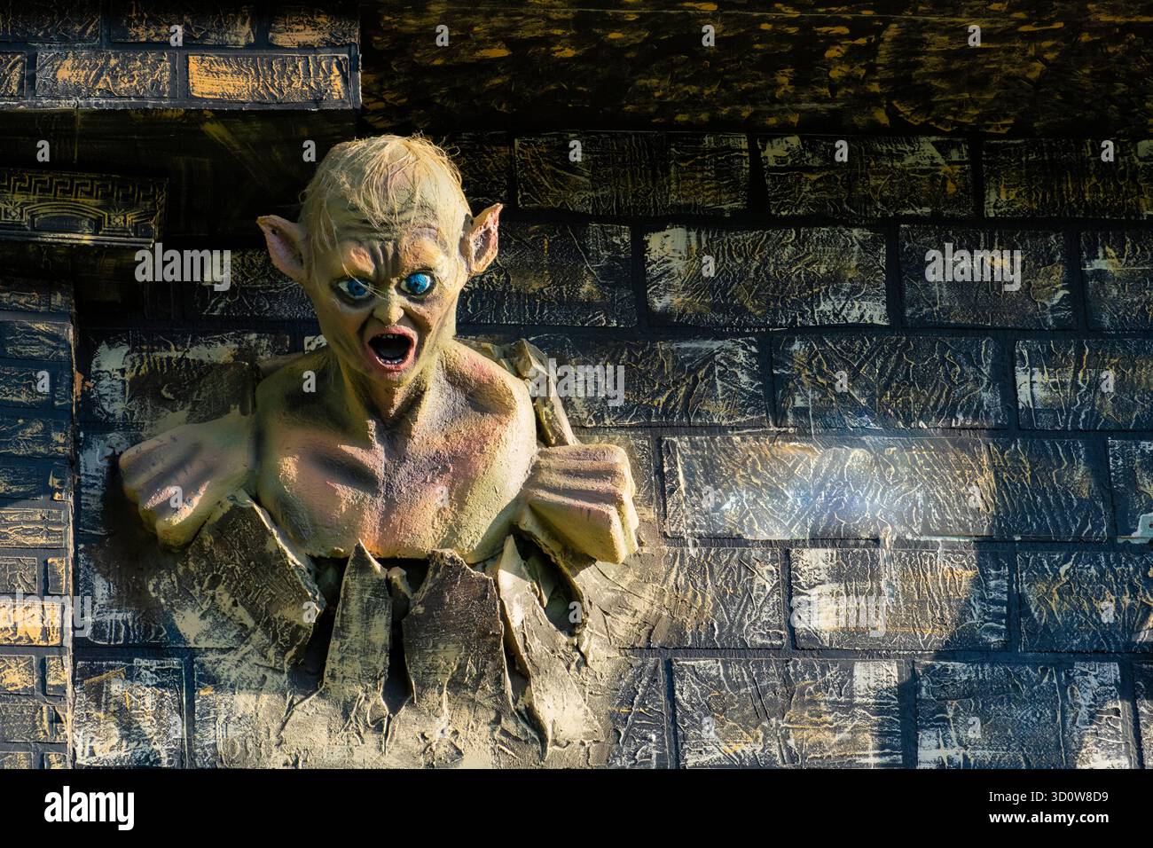 Scultura drammatica di una figura mostruosa che irrompe attraverso una parete di mattoni con occhi vivaci e bocca aperta, perfetta per fantasia, Halloween o decorazioni a tema Foto Stock