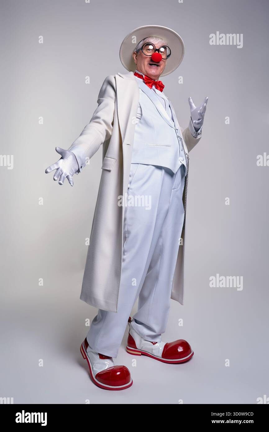 Un clown anziano con un cappotto bianco e un cappello. L'uomo indossa grandi stivali da clown in pelle verniciata rossa. Foto Stock