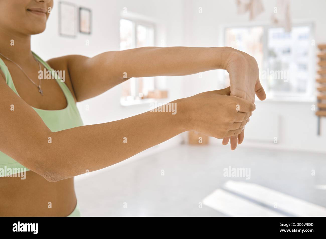 Una persona sta eseguendo un allungamento del braccio in uno spazio interno luminoso, promuovendo flessibilità e relax. La luce del sole riempie la stanza, creando un'atmosfera tranquilla Foto Stock