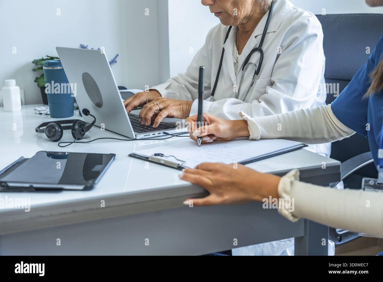 Team medico composto da un medico e un infermiere che lavorano insieme sui file dei pazienti, con uno che digita su un computer portatile e l'altro che scrive appunti, dimostratina Foto Stock
