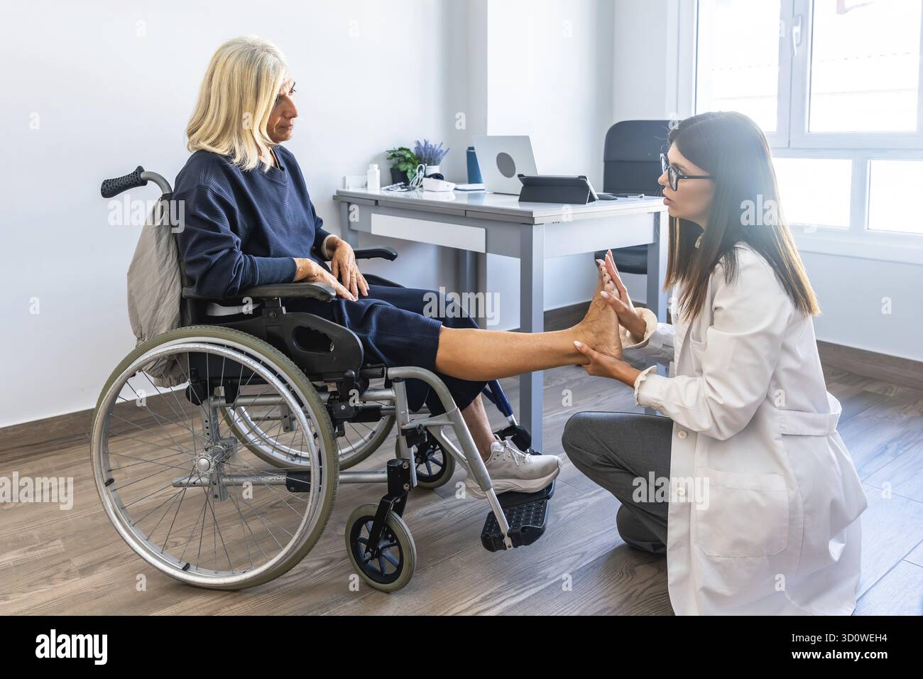 Medico donna che esamina il piede di una donna anziana durante una sessione di riabilitazione, concentrandosi sulla fisioterapia e l'assistenza sanitaria per le persone con d Foto Stock