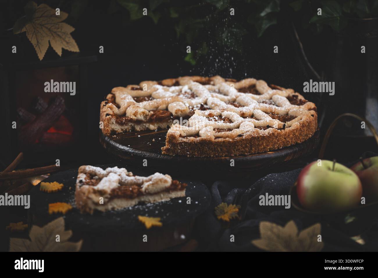 Lo zucchero a velo cade sulla torta di mele circondata da foglie autunnali in un ambiente buio Foto Stock