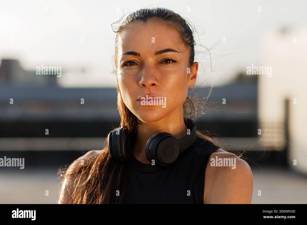 Primo piano ritratto dettagliato di una giovane donna sportiva dalla pelle liscia, con cuffie wireless e in piedi all'aperto Foto Stock
