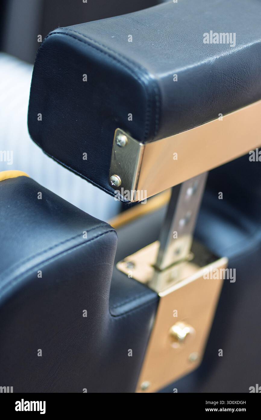 Primo piano di una sedia da barbiere nera e dorata dall'angolo posteriore sinistro, riprodotta in verticale con dettagli eleganti. Foto Stock