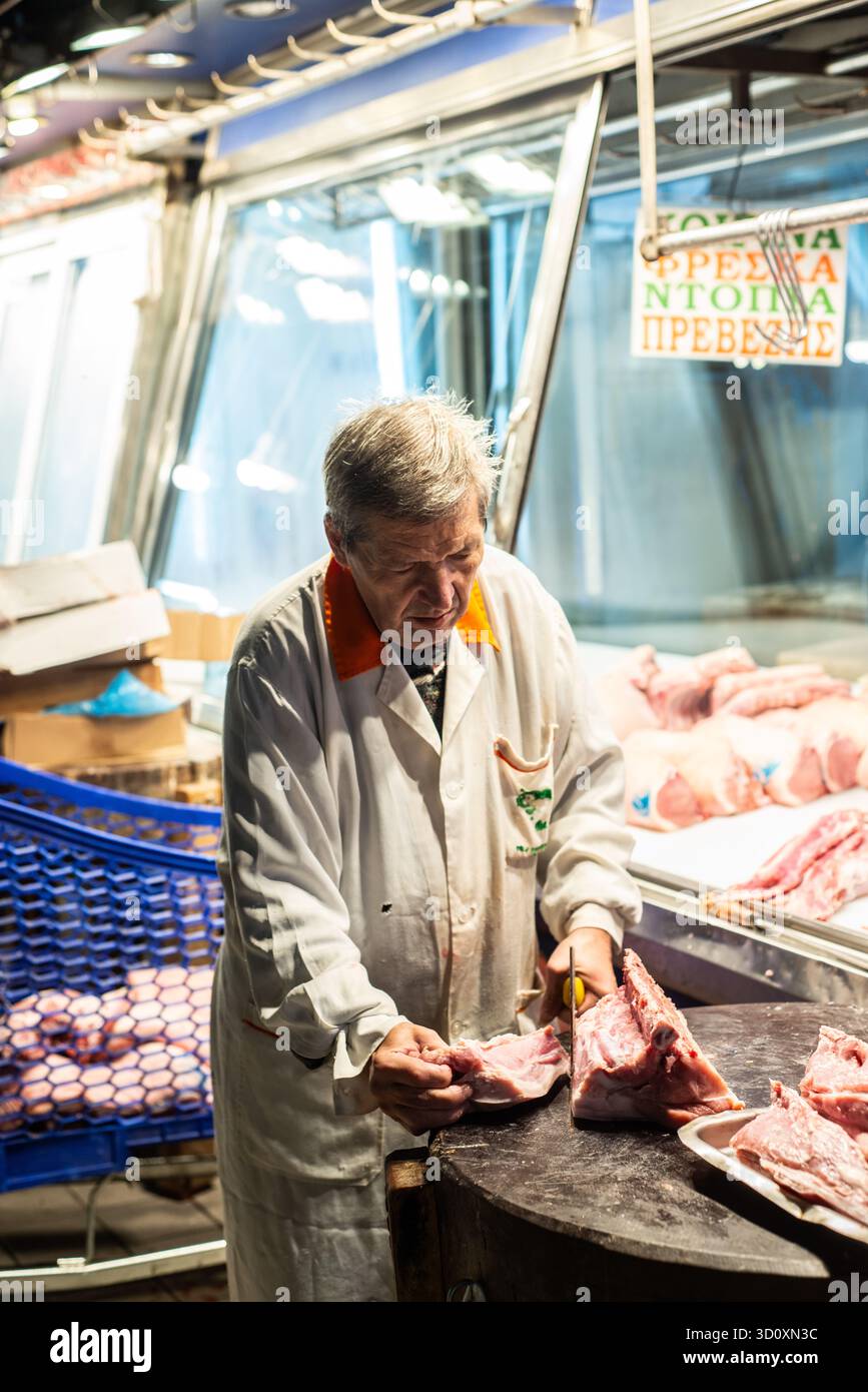 Un macellaio prepara tagli di carne per la vendita durante i primi momenti di apertura del mercato centrale di Atene, Grecia. Foto Stock