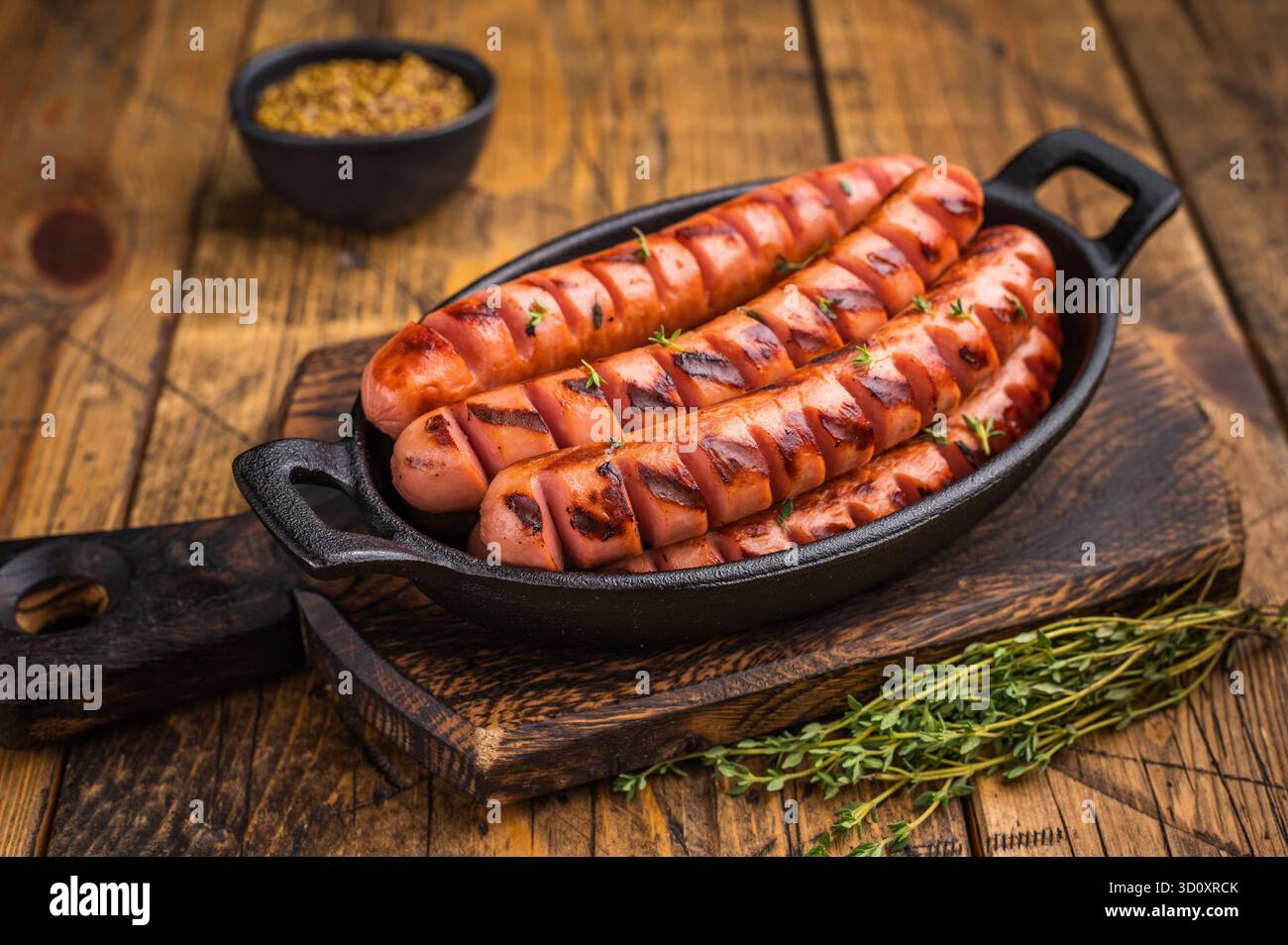 Salsicce fritte succose affumicate su un asse di legno con erbe e forchetta. Immagine di alta qualità per i menu dei ristoranti o le intestazioni dei blog di cibo Foto Stock
