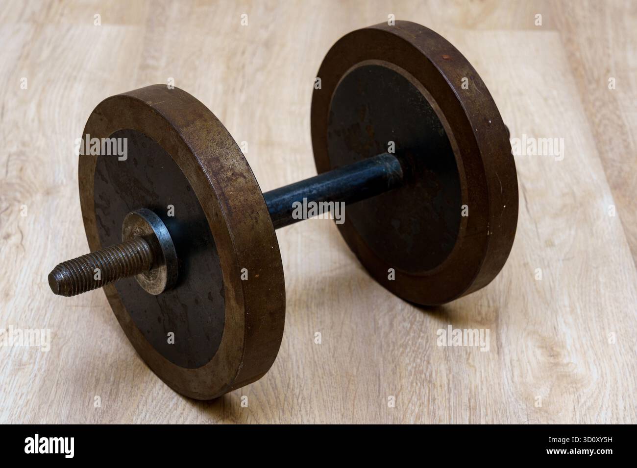 Un manubrio con pesi usurati siede su un pavimento di legno, mostrando segni di uso frequente in un ambiente di palestra domestico. Foto Stock