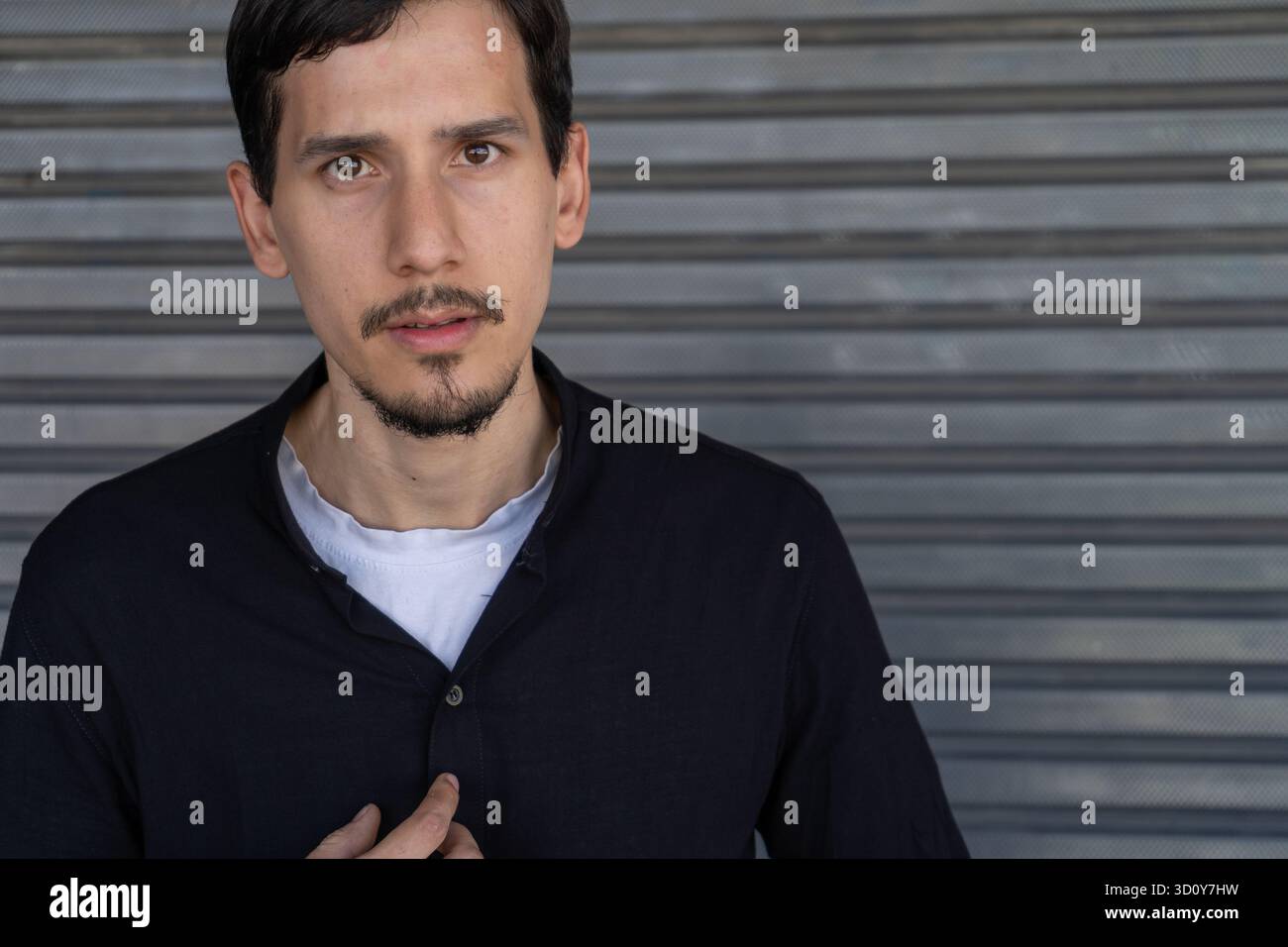 Giovane uomo in piedi, indossa una camicia scura, che entra in contatto visivo con un'espressione seria e contemplativa Foto Stock