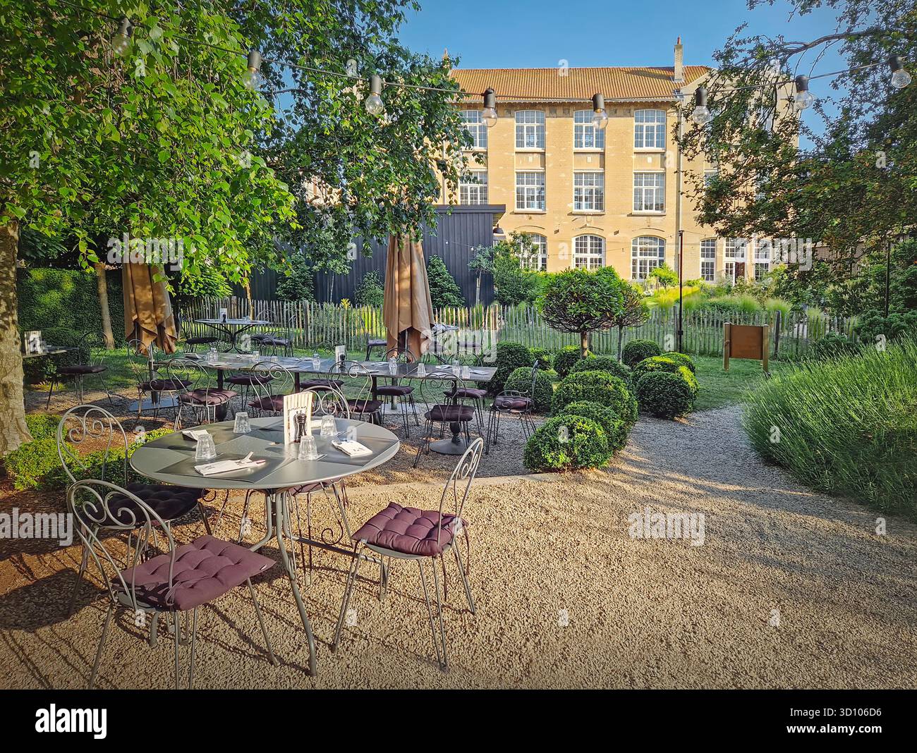 Terrazza ristorante rustica all'aperto con un'estetica classica ed europea del giardino. L'area salotto presenta tavoli da bistrot rotondi disposti su un sentiero di ghiaia. Strin Foto Stock