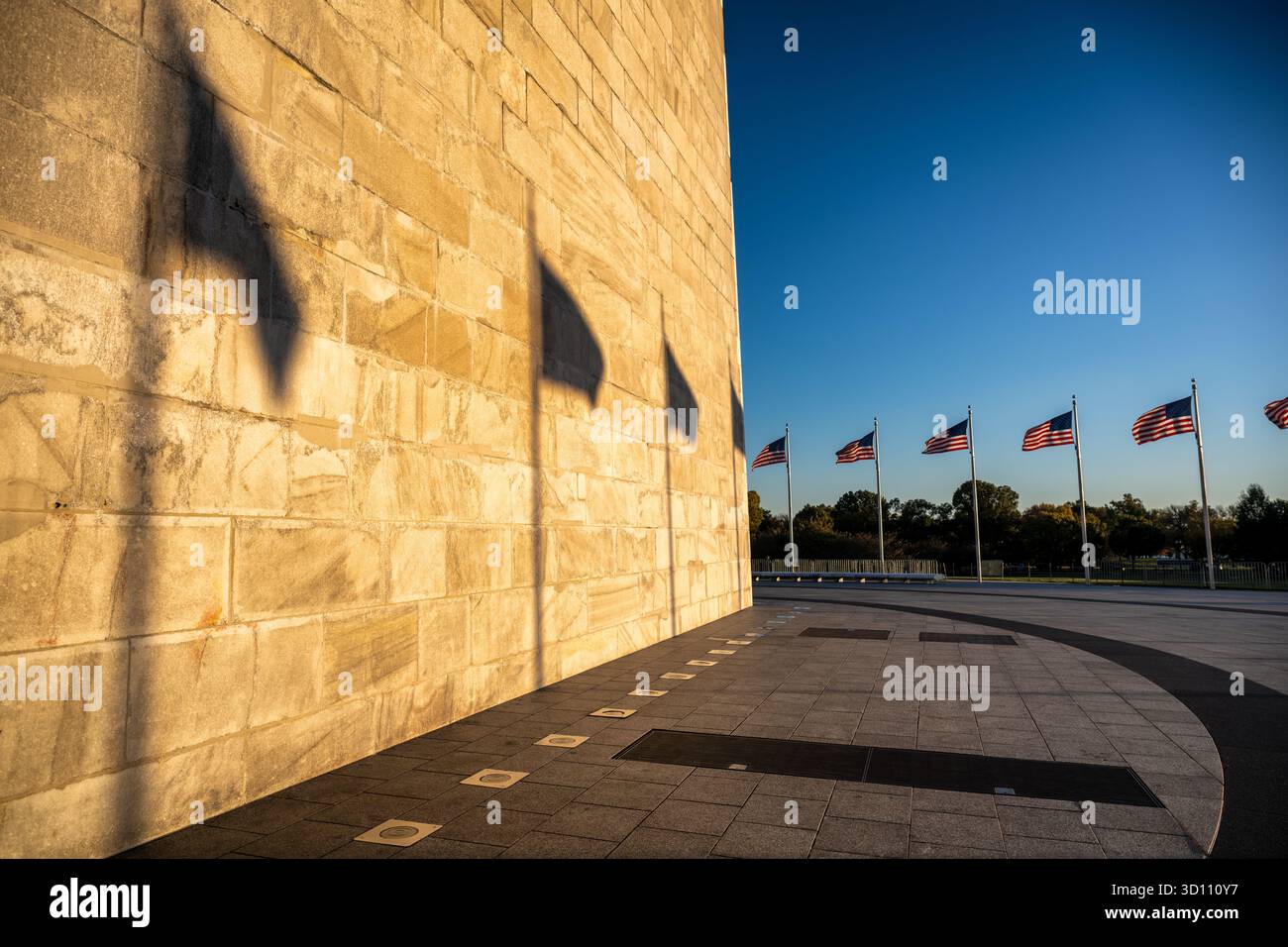 Monumento a Washington con le ombre della bandiera al tramonto Washington DC // WASHINGTON DC - il monumento a Washington, un obelisco in onore di George Washington, è immerso nella calda luce del sole che tramonta. Le lunghe ombre delle bandiere americane e dei loro pali sono gettate sull'esterno del monumento, costruito in marmo, granito e gneiss di pietra blu. Alto 169,29 metri (555 piedi e 1/8 pollici), questo iconico monumento è circondato da un anello di 50 bandiere americane. È una caratteristica centrale del National Mall, che simboleggia la capitale della nazione. Foto Stock