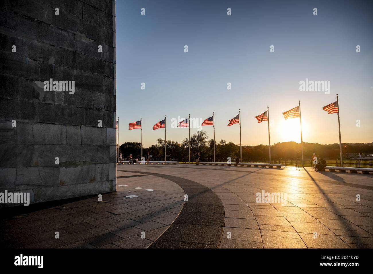 Washington Monument Flags al tramonto Washington DC // WASHINGTON DC - il monumento a Washington si vede al tramonto, bagnato da un bagliore dorato mentre il sole si abbassa all'orizzonte. Un'esposizione di bandiere americane, in genere volate 24 ore al giorno, traccia il percorso, con 50 bandiere che rappresentano i 50 stati. Questo iconico monumento nazionale, alto 169 metri (555 piedi), onora George Washington, il primo presidente degli Stati Uniti, ed è la struttura in pietra e l'obelisco più alti del mondo. Il sole che tramonta getta lunghe ombre dalle bandiere, creando una scena drammatica e patriottica. Foto Stock