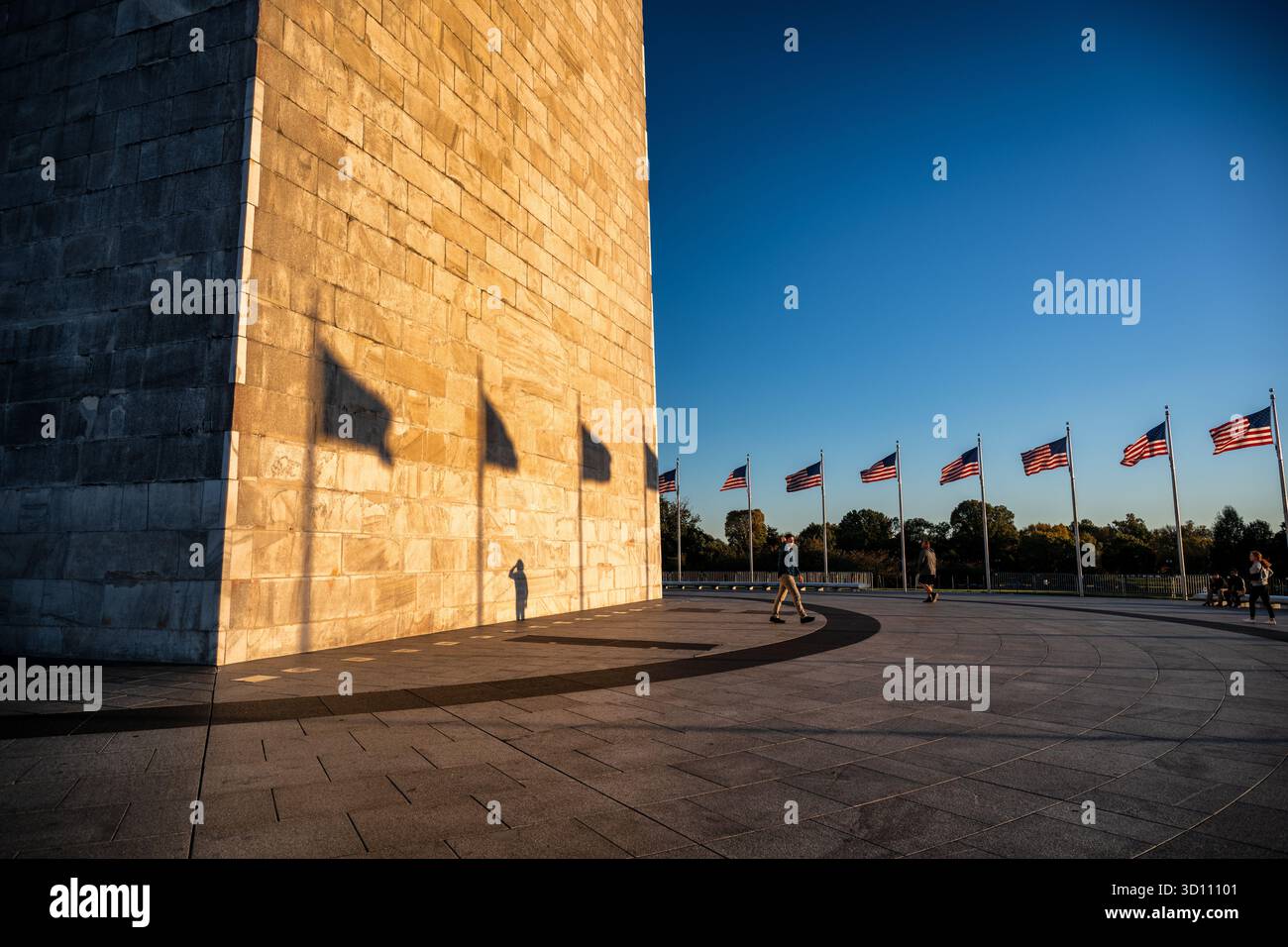 Monumento a Washington con le ombre della bandiera al tramonto Washington DC // WASHINGTON DC - il monumento a Washington è illuminato dal sole che tramonta, gettando ombre delle bandiere americane sulla sua facciata in pietra dalle tonalità dorate. Questo iconico obelisco onora George Washington, il primo presidente degli Stati Uniti, e si trova nel National Mall. È la struttura in pietra più alta del mondo, alta 169,046 metri (554 piedi 7 11/32 pollici). Costruito in marmo, granito e gneiss di pietra tra il 1848 e il 1884, è circondato da 50 bandiere americane. Foto Stock
