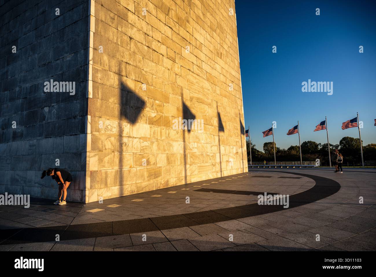 Monumento a Washington con le ombre della bandiera e il tramonto d'oro Glow Washington DC // WASHINGTON DC - il monumento a Washington è immerso nel bagliore dorato del sole che tramonta, con la sua facciata in pietra che getta lunghe e drammatiche ombre delle circostanti bandiere americane. Questo iconico obelisco, un tributo a George Washington, il primo presidente degli Stati Uniti, è una struttura torreggiante di marmo, granito e gneiss di pietra blu. Con un'impressionante altezza di 169,046 metri (554 piedi e 7 pollici), è circondato da 50 bandiere americane, ognuna delle quali rappresenta uno stato dell'Unione. Situato sul National Mall, questo punto di riferimento è un importante centro commerciale Foto Stock