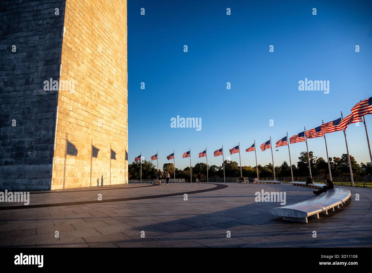 Monumento a Washington con bandiere americane al tramonto Washington DC // WASHINGTON DC - il monumento a Washington è illuminato dal sole che tramonta, gettando lunghe ombre dalle bandiere americane circostanti sulla sua base. Questo iconico obelisco, costruito in marmo, granito e gneiss di pietra blu, commemora George Washington, il primo presidente degli Stati Uniti. Con un'altezza di 555 piedi e 1/8 pollici (169,294 metri), è la struttura in pietra più alta del mondo e l'obelisco più alto, che funge da punto di riferimento centrale nel National Mall di Washington DC. Foto Stock